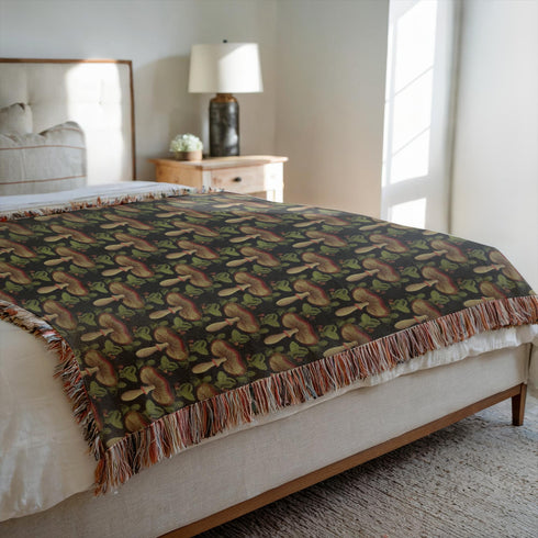 A woven cotton throw featuring an intricate mushroom and foliage pattern in deep charcoal and golden hues, framed by soft fringe.